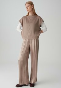 Bordeaux platte schoenen, crèmekleurig langemouwen top onder een korte, beige satijnen blouse en wijde beige satijnen broek. Gladde textuur, modern ontwerp.