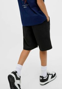 Shorts noirs avec une coupe décontractée, poches, associés à des chaussettes blanches et des baskets noir et blanc. Le T-shirt est bleu marine avec des graphiques imprimés.