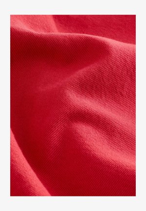 Tessuto rosso con un motivo intrecciato e testurizzato, che mostra pieghe e una superficie liscia. Il colore è uniforme e vivido in tutto il tessuto.