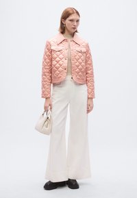 Ροζ τζιν μπουφάν με επένδυση και γιακά, φορεμένο πάνω από ένα μπεζ τοπ και λευκό παντελόνι με φαρδιά μπατζάκια. Κρατάει μια μικρή κρεμ τσάντα χιαστί, με μαύρα χοντρά μποτάκια.