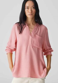 Camicia rosa chiaro a maniche lunghe con colletto senza bottoni, taschino sul petto e maniche arrotolate, realizzata in tessuto testurizzato.