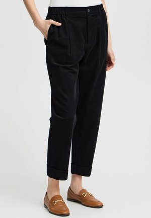 Pantalon en velours côtelé noir avec une coupe décontractée, des plis à l'avant, des poches latérales et des ourlets retroussés, associé à des mocassins marron.