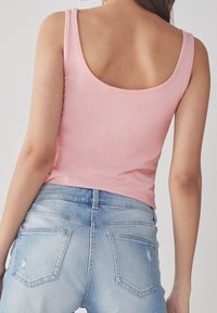 Top sin mangas de color rosa claro con espalda en forma de scoop, combinado con jeans de mezclilla. Presenta un diseño ajustado y una textura suave.