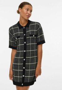 Robe à carreaux noir et blanc avec un col, des manches courtes, un devant à boutons et deux poches poitrine, confectionnée dans un tissu tricoté texturé.