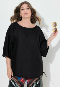 Top nero, dalla vestibilità ampia, con scollatura rotonda e maniche lunghe. Abbinato a pantaloni colorati con motivo, che presentano dettagli floreali.