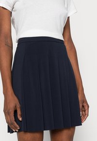 Marinblå veckad kjol som är tillverkad av mjukt tyg med midja som sitter tajt. Har flera vertikala veck och en slät yta.