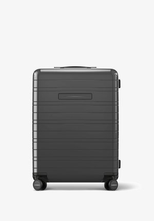 Valise rigide de couleur gris foncé, avec un design rainuré, une poignée supérieure, une poignée latérale et quatre roulettes noires pivotantes pour la mobilité.