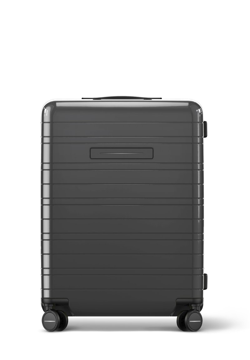 Valise rigide de couleur gris foncé, avec un design rainuré, une poignée supérieure, une poignée latérale et quatre roulettes noires pivotantes pour la mobilité.