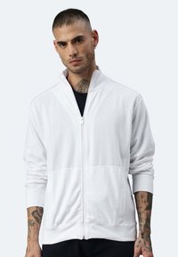Weiße Zip-Jacke aus weichem Stoff, mit hohem Kragen, gerippten Bündchen und glatter Textur. Details umfassen Seitentaschen und Nähte.