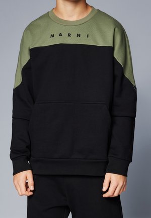 Osoba ubrana w czarno-oliwkową bluzę z logo "MARNI" na piersi, stojąca na jednolitym szarym tle.