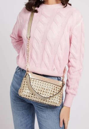 Proplétaná zlatá kabelka s hladkým kovovým páskem, vybavená zakřiveným vrškem a texturovaným tělem. Doplněná světle růžovým svetrem s kabelovým vzorem.