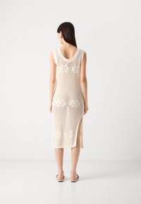 Knit dress in cream, featuring a floral pattern, wide neckline, and side slits. Made of breathable material for summer wear.