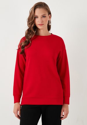 Felpa rossa a maniche lunghe in materiale a costine con collo rotondo e vestibilità rilassata, abbinata a pantaloni neri con una texture liscia.