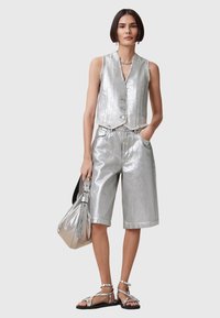 Metallic silver vest and shorts with a textured finish, featuring a button closure, side pockets, and sleek sandals. Accompanied by a silver bag.