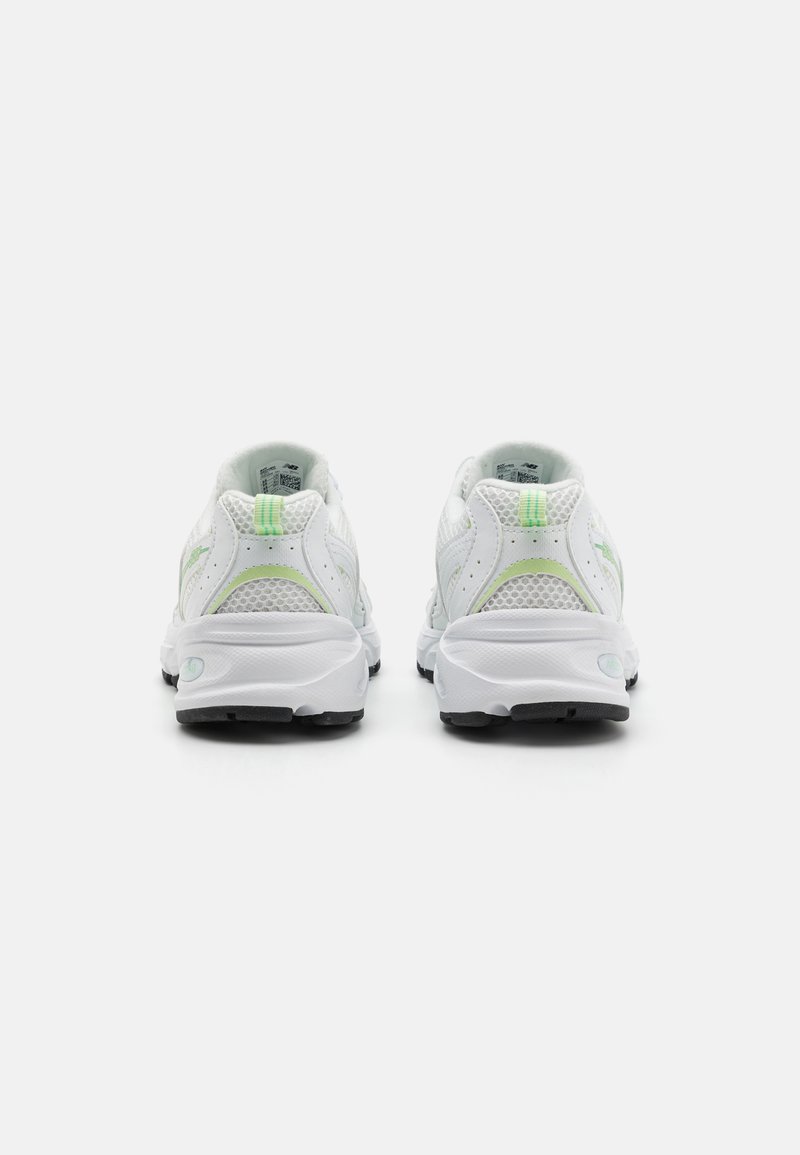 Zapatillas deportivas blancas con parte superior de malla, detalles en verde, cuello acolchado y suela negra texturizada con una ligera elevación en el talón.