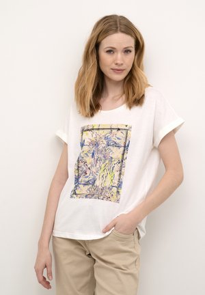 T-shirt blanc à manches courtes avec un imprimé abstrait coloré au centre ; col rond et coupe décontractée. Associé à un pantalon beige clair.