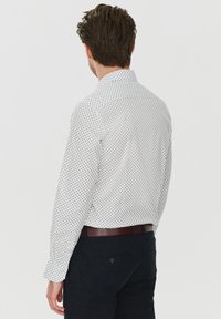 Biała koszula z małymi niebieskimi kropkami, z zapięciem na guziki przy kołnierzyku, długie rękawy i regularny krój, w połączeniu z ciemnymi spodniami i brązowym paskiem.