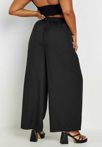 Svarta vida byxor med vita prickar, med ett elastiskt midjeband och lätt tyg. I kombination med svarta blockklacksandaler.