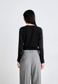 Musta pitkähihaista puseroa, jossa on sileä pinta, yhdistettynä vaaleanharmaisiin raidallisiin leveälahkeisiin housuihin, joissa on etutaskut ja laskokset.