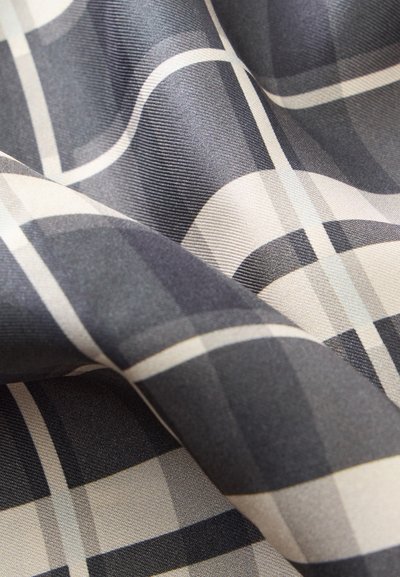 Gros plan d'un tissu froissé avec un motif à carreaux noir, blanc et gris présentant des lignes croisées.