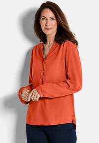 Blusa arancione brillante con scollatura a V, patta con bottoni frontale, maniche lunghe e spacchi laterali. Texture liscia e tessuto morbido.