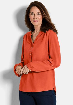Helles orange Blusenshirt mit V-Ausschnitt, Knopfleiste vorne, langen Ärmeln und seitlichen Schlitzen. Glatte Textur und weicher Stoff.