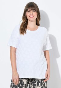 Top bianco a maniche corte con texture floreale e scollatura tonda. Il tessuto sembra morbido, abbinato a pantaloni neri a fantasia con disegni astratti.