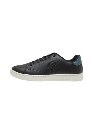 Zapatilla baja de cuero negro con cordones negros, suela blanca, lengüeta verde en el talón y logotipo circular en relieve en el lateral.
