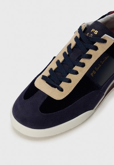 Sneaker in camoscio blu navy e beige con lacci blu navy, suola bianca e marchio "PS Paul Smith" in oro sul lato e sulla linguetta.