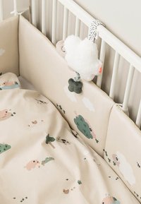 Wieg met beige gevoerde zijkanten met schattige patronen van dieren en bomen. Gehecht pluchen wolkenspeeltje met een groen accent en een polkadot bandje.