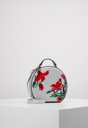 Sac à main rond gris clair avec une petite anse, une bandoulière et une broderie florale rouge éclatante sur le devant, posé sur une surface blanche.