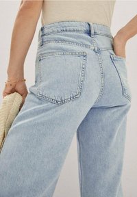 Jean bleu clair taille haute à coupe décontractée, avec deux poches arrière et un effet délavé, associé à un haut beige texturé.