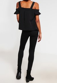 Top nero scollato con spalline larghe e dettagli di volant, abbinato a jeans skinny neri e stivali alla caviglia. Tessuto morbido e design aderente.