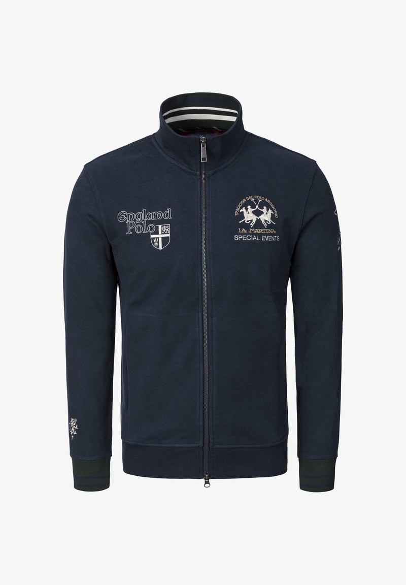 Mörkblå zip-up jacka i fleece, med broderade logotyper och randig krage. Ribbstickade muddar med gröna och blå accenter.