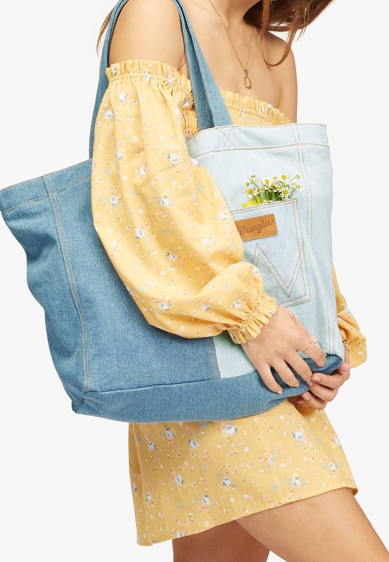 Torba na ramię z denimu w jasnoniebieskich i ciemnoniebieskich sekcjach, z przednią kieszenią ozdobioną kwiatami. Miękka w dotyku i o dużej pojemności.