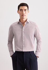 Camicia con colletto a righe sottili rosse e bianche, maniche lunghe e bottoni bianchi; indossata con pantaloni scuri. Tessuto dalla trama liscia.