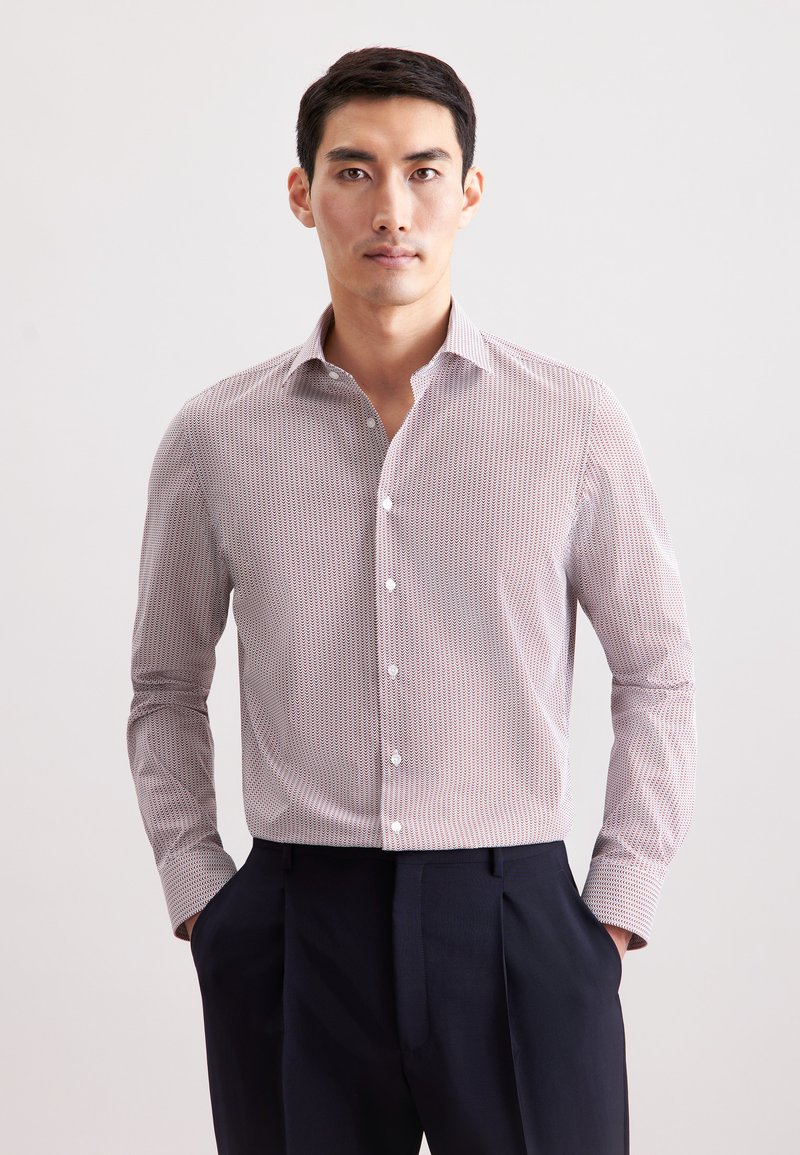 Camicia con colletto a righe sottili rosse e bianche, maniche lunghe e bottoni bianchi; indossata con pantaloni scuri. Tessuto dalla trama liscia.