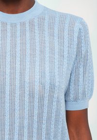 Ljusblå stickad topp med korta puffärmar, med vertikala ränder och mönstrad struktur. Tillverkad av mjukt, andningsbart tyg.