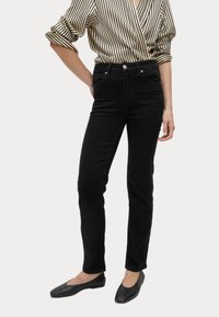Jeans de mezclilla negros con corte slim, que cuentan con un diseño clásico de cinco bolsillos y cinturilla con botón. Se llevan con una blusa a rayas y zapatos planos.
