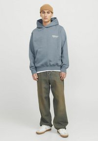 Sudadera con capucha gris de algodón, con un bolsillo frontal y texto en blanco. Combinada con jeans de denim sueltos y desgastados y zapatillas blancas.
