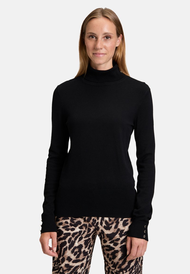 Fekete garbó pulóver hosszú ujjakkal, bordás mandzsettával és testhezálló fazonnal. Mintás állatmintás nadrággal viselve, bézs és barna árnyalatokkal.