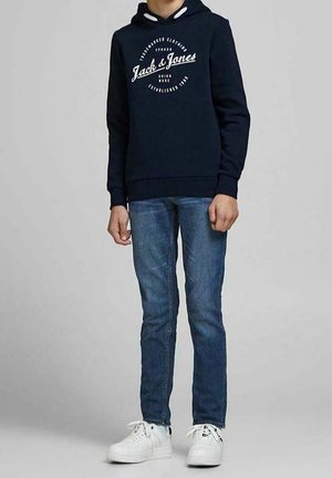 Sweat à capuche bleu marine avec logo sur le devant, associé à un jean en denim bleu et des baskets blanches. Le sweat à capuche est doté d'un cordon de serrage et de poignets côtelés.