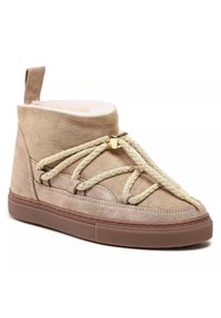 Beige suède hoge sneakers met een gewatteerde kraag, creamkleurige faux fur voering, dikke beige veters en een gouden metalen accent aan de voorkant. Bruine rubberen zool.