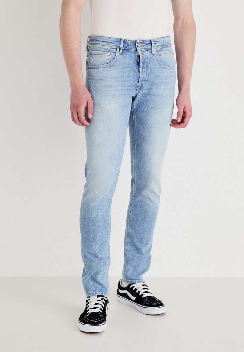 Lyseblå denimjeans med slim fit, med fem lommer, subtil falming, og paret med svarte sneakers med hvite detaljer.