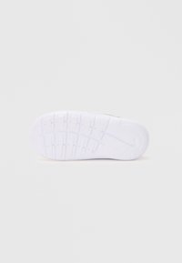 Semelle de sneaker blanche en caoutchouc texturé, avec un design ondulé, des rainures pour l'adhérence et un accent circulaire près du talon.