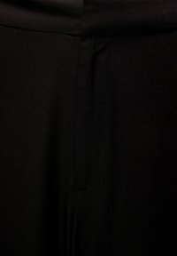 Zwarte stoffen broek met een gladde textuur en centrale zakdetails. De tailleband is plat, wat zorgt voor een gestroomlijnd uiterlijk.