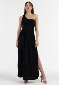 Rochie maxi neagră, cu un singur umăr, cu un design drapat, bust ajustat și fustă fluidă. Are o fanta laterală și este purtată cu sandale cu barete.
