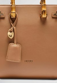 Borsa in pelle marrone chiaro con manici in bambù, accessori in oro e un'etichetta a forma di cuore. Presenta il logo "LIU JO" in rilievo e una superficie liscia.
