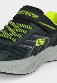 Baskets Skechers gris foncé et vert néon avec lacets à motifs, bride velcro, empeigne en mesh et semelle blanche coussinée, vues en gros plan.
