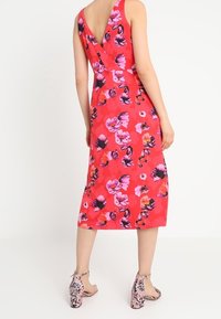 Abito floreale in un vivace rosa con motivi di fiori variabili in viola e rosa. Presenta un design con scollo a V e un taglio fino al ginocchio, abbinato a tacchi floreali.